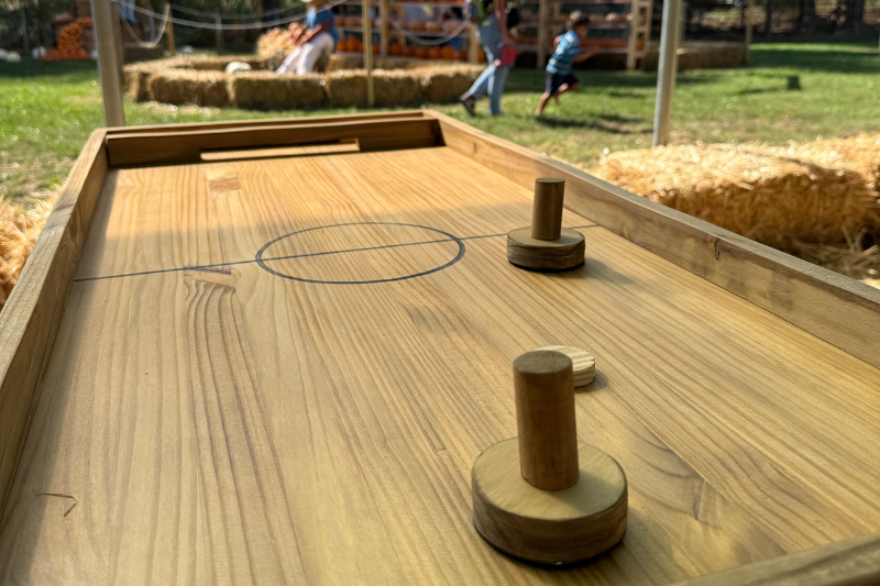 Mano che tiene una zucca di Halloween intagliata con volto sorridente e denti bianchi, con visitatori dell'evento sullo sfondo in un'area con gazebo e alberi
