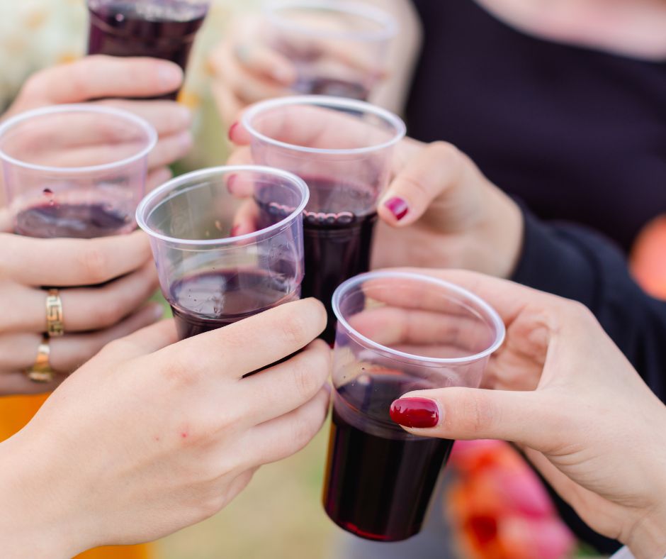 Brindisi tra più persone con bicchieri di plastica trasparenti pieni di vino rosso